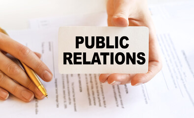 Business woman sitting at a table in a light office holding a business card. The content of the lettering has implications for business concept and marketing. Close-up, soft light.