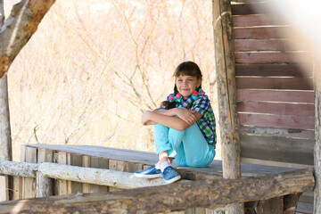 A ten-year-old girl sits in a wooden gazebo and looks cheerfully into the frame