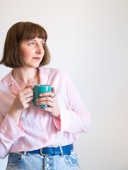 Young woman wearing pink shirt drinking coffee and smiling over white wall background.