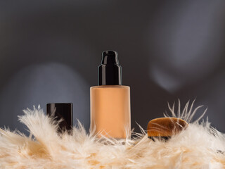 Unbranded generic foundation bottle with feathers and professional brush on dark gray background...