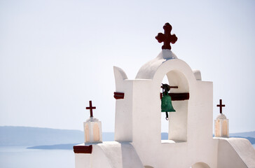 A tower top of a church with cross sign and bells architecture located in oia village in one of...
