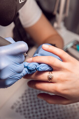 Manicure master doing manicure in blue gloves for client with a Electric Nail File Drill Machine. Female hardware manicure in the salon. Electric nail file for trimming and removing cuticles.