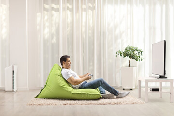 Young man sitting on a green bean bag and playing video games with a joystick