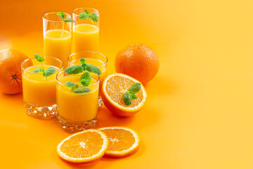 Fresh oranges and orange juice in glasses on an orange background. Mint leaves. Still life. close-up. Copy space.