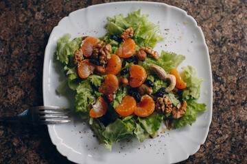 Close-up of tangerines, fresh lettuce salad and nuts top view