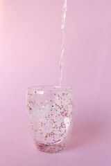 Glass of water with colorful stars on pink background, water drops filling