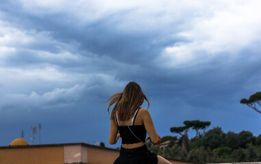 girl sitting with her back against the background of an incredibly beautiful sky in Rome 