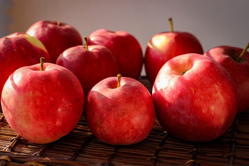 Several ripe red apples stand on a wicker basket illuminated by rays of the sun