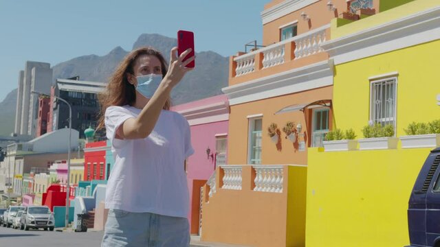 Woman tourist in pandemic shoots on the phone in Cape town Bo-Kaap Malay area, perspective of cobble stone street, colored terrace houses, South Africa.