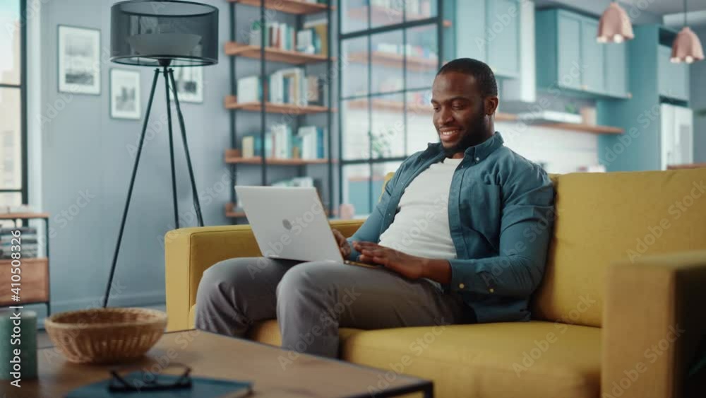 Poster handsome black african american man working on laptop computer while sitting on a sofa in cozy livin