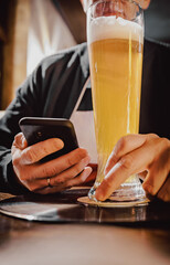 close up of man hand hold smartphone, drinking beer and reading message at bar or pub