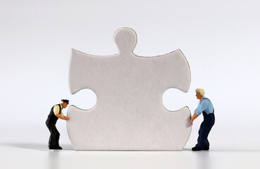 Two miniature men carrying puzzle piece. Puzzle pieces and miniature people.