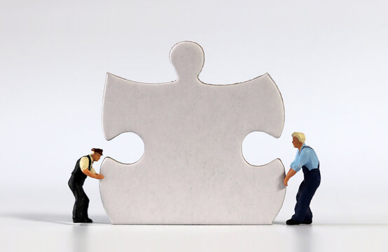 Two miniature men carrying puzzle piece. Puzzle pieces and miniature people.

