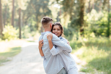 Fototapeta premium Cheerful young woman and man are hugging outdoors in summer park. Dating and romantic vacation. couple in love gently looking at each other on sunny day. Love and relationships between young people