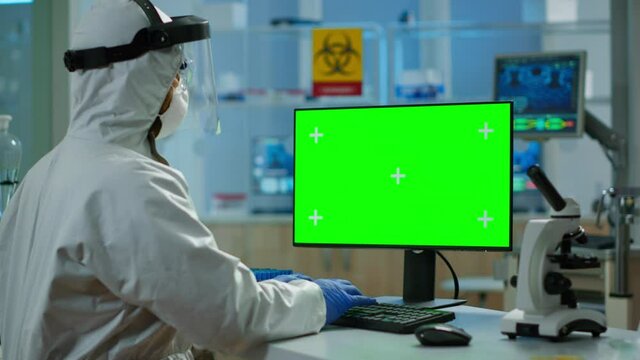 Man researcher in coverall looking at chroma key computer in modern equipped lab. Team of microbiologists doing vaccine research writing on device with green screen, isolated, mockup display.