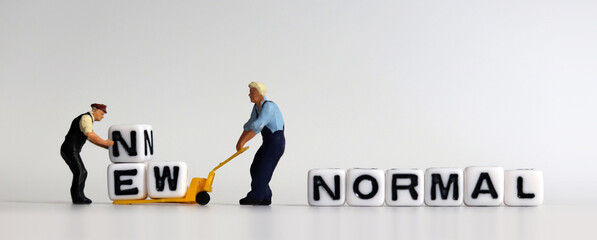 New Normal concept. Two miniature men carrying NEW on a cart. 
