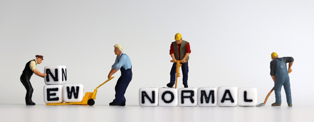 The concept of preparing a New Normal. Two miniature men carrying NEW on a cart. 
