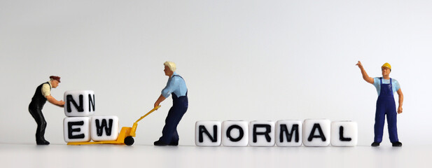 The concept of preparing a New Normal. Two miniature men carrying NEW on a cart. 
