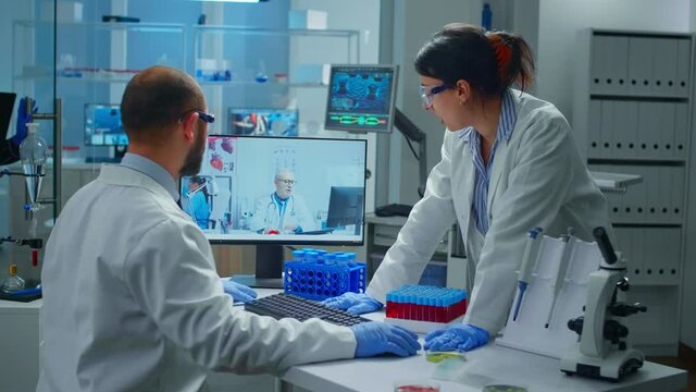Lab technicians talking on video call with professional chemist doctor explaning vaccine reactions, woman nurse showing blood sample on web cam, during virtual meeting in medical research laboratory