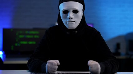 Nervous stressed unrecognizable hacker in black clothes and anonymous mask beating table with fists. Anxious man failing in hacking or coding online virus.