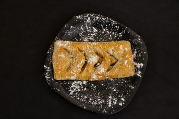 sweet delicious pie sprinkled with powdered sugar on a black plate