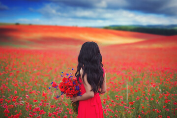 Beautiful Asian girl with long hair in a red dress with a large bouquet of poppies and cornflowers in her hands on the background of a blooming field with wild red flowers.
