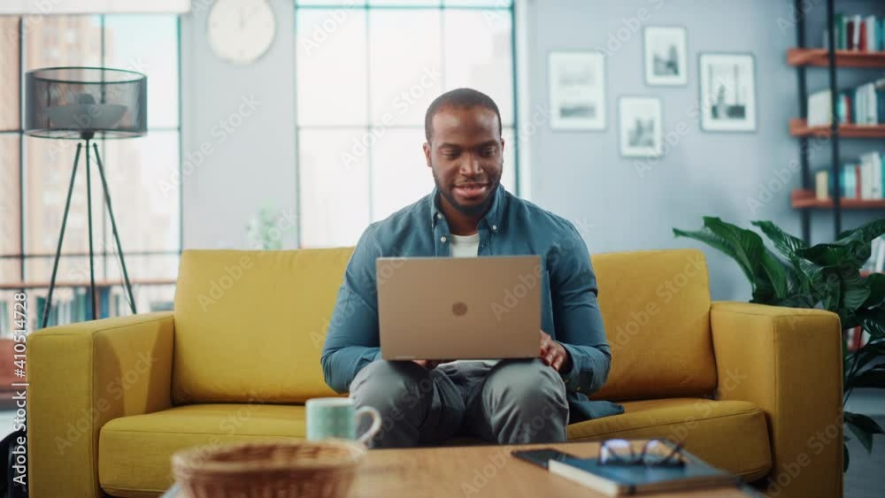 Poster handsome black african american man working on laptop computer while sitting on a sofa in cozy livin