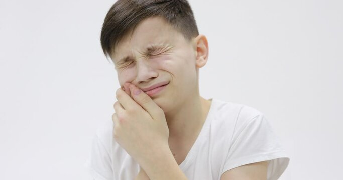 Child toothache. holding his cheek, dental pain. Closeup portrait boy with sensitive tooth. isolated white wall background. Negative human emotion, facial expression feeling reaction
