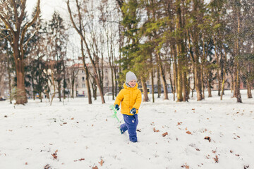 Little boy in a walk in the park with his family in winter, having fun and enjoying the snow