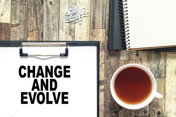 Text Change and Evolve with cofee cup, book,notepad,pen and pencils on the wooden background. Business concept.