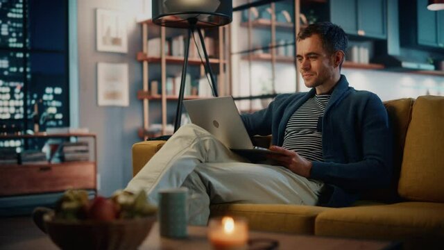 Handsome Caucasian Man Having a Video Call on Laptop Computer while Sitting on a Sofa in Cozy Living Room
