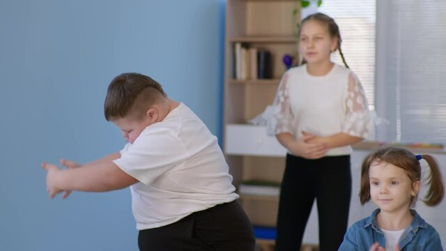 active hobbies, chubby boy child with down syndrome dancing with a group of healthy children during a dance lesson closeup