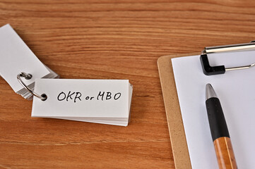 There's a clipboard, a pen and a wordbook stuck to it that says OKR or MBO.