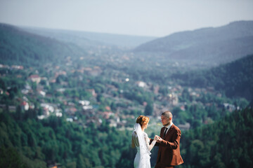 happy stylish bride and groom running and having fun in mountains on summer sunny day. gorgeous newlywed couple laughing, true feelings. emotional romantic moment.