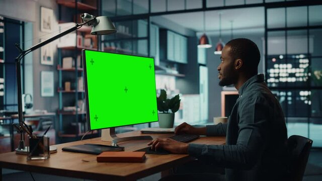 Handsome Black African American Specialist Working on Desktop Computer with Green Screen Mock Up Display at Home Living Room. Freelance Man Chatting to Clients Over the Internet on Social Networks.