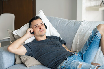 Fototapeta premium the guy enjoys the music while lying on the couch with headphones. Relaxation with music