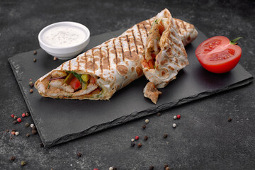 Shawarma with meat, cutaway, with sauce, tomatoes, cheese, herbs and garlic, on black slate, on a black background