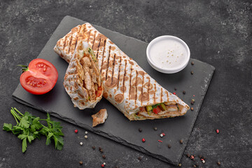 Shawarma with meat, cutaway, with sauce, tomatoes, cheese, herbs and garlic, on black slate, on a...