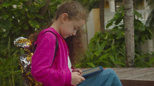 Plays in the phone sitting on street alone.Children tech addiction concept play game. Cute little girl child using a digital tablet technology device telephone or laptop.
