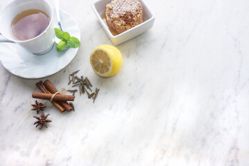 A cup of green tea with flavouring spices of cinnamon,anise,honey,peppermint on a textured marble background with copy space.