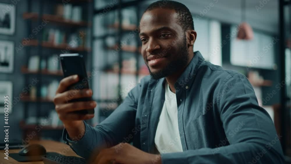 Poster excited black african american man using smartphone while sitting at table in living room. happy man