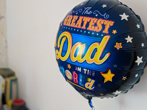 Closeup Of Blue Helium Balloon Saying Greatest Dad In Bokeh Background.