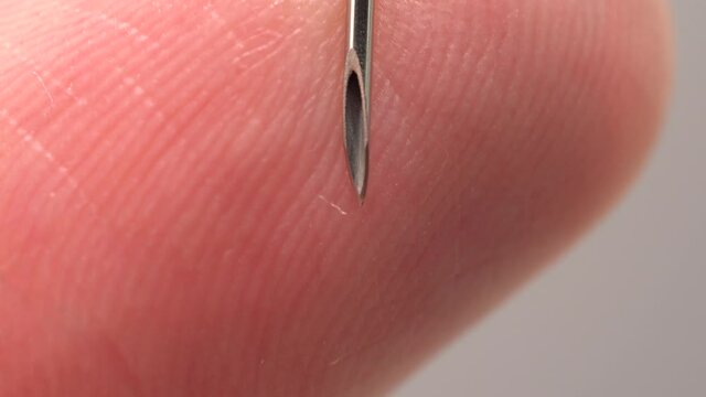 Finger touching medical syringe needle. Macro close up. Trypanophobia, extreme fear of injections or hypodermic needles. Dangerously close hand skin to the sharp needle. Phobias and traumas.