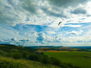 Landscape photo with clouds green fields hills an glider in sky.