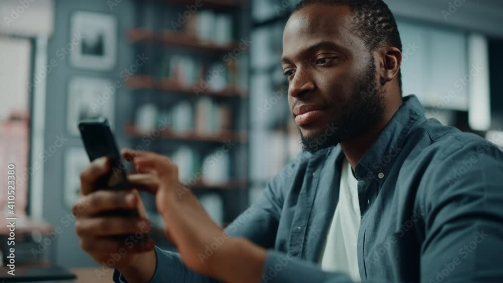 Poster excited black african american man using smartphone while sitting at table in living room. happy man