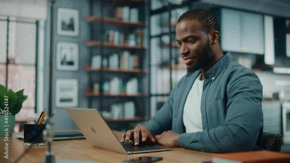 Poster handsome black african american man working on laptop computer while sitting behind desk in cozy liv