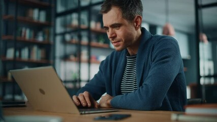 Handsome Caucasian Man Working on Laptop Computer while Sitting Behind Desk in Cozy Living Room. Freelancer Working From Home. Browsing Internet, Using Social Networks, Having Fun in Flat.