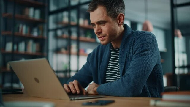 Handsome Caucasian Man Working on Laptop Computer while Sitting Behind Desk in Cozy Living Room. Freelancer Working From Home. Browsing Internet, Using Social Networks, Having Fun in Flat.
