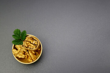 Peeled walnuts in a round wooden bowl on a gray background.