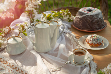 Coffee set on a white tablecloth on a sunny day, cherry blossom, cupcake, pudding, chocolate, cocoa. Outdoor, picnic, brunch, spring mood. Soft focus